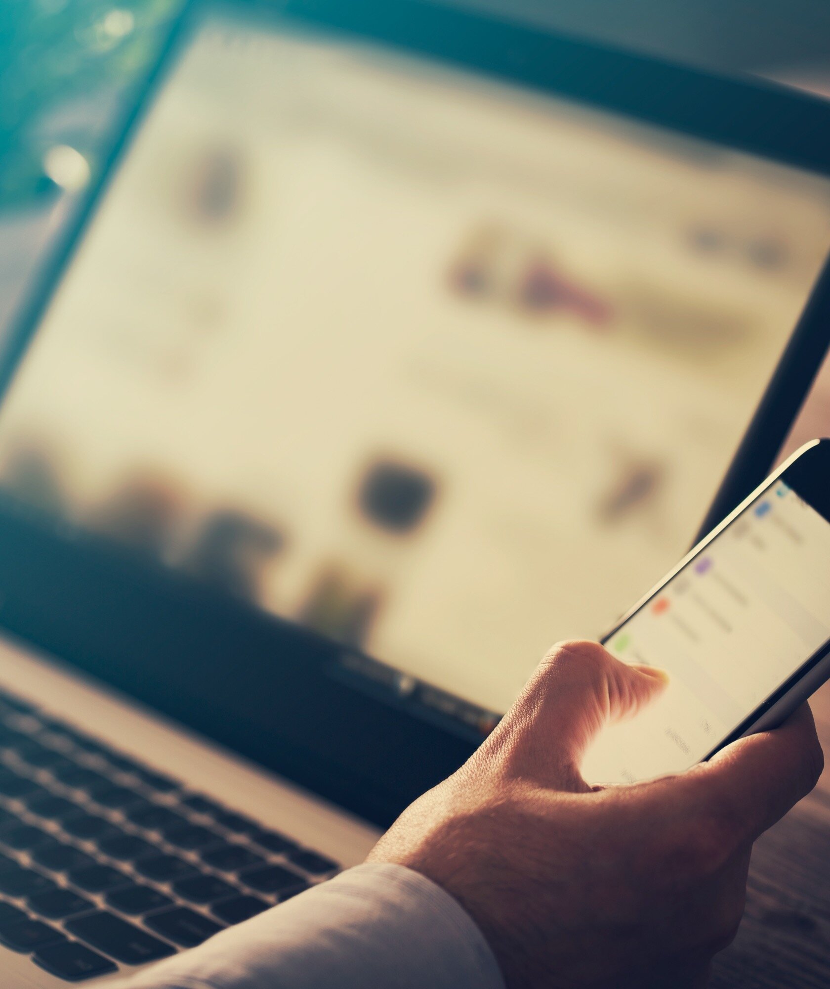 Person completing new patient forms online on a laptop while holding a smartphone