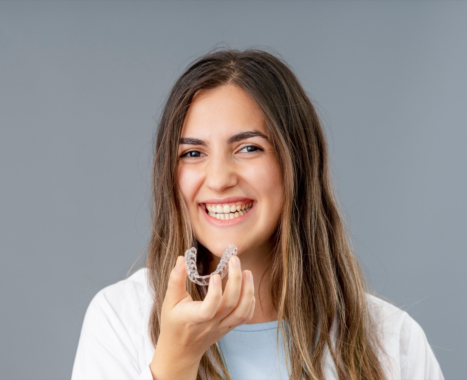 Smiling young woman holding a clear aligner tray