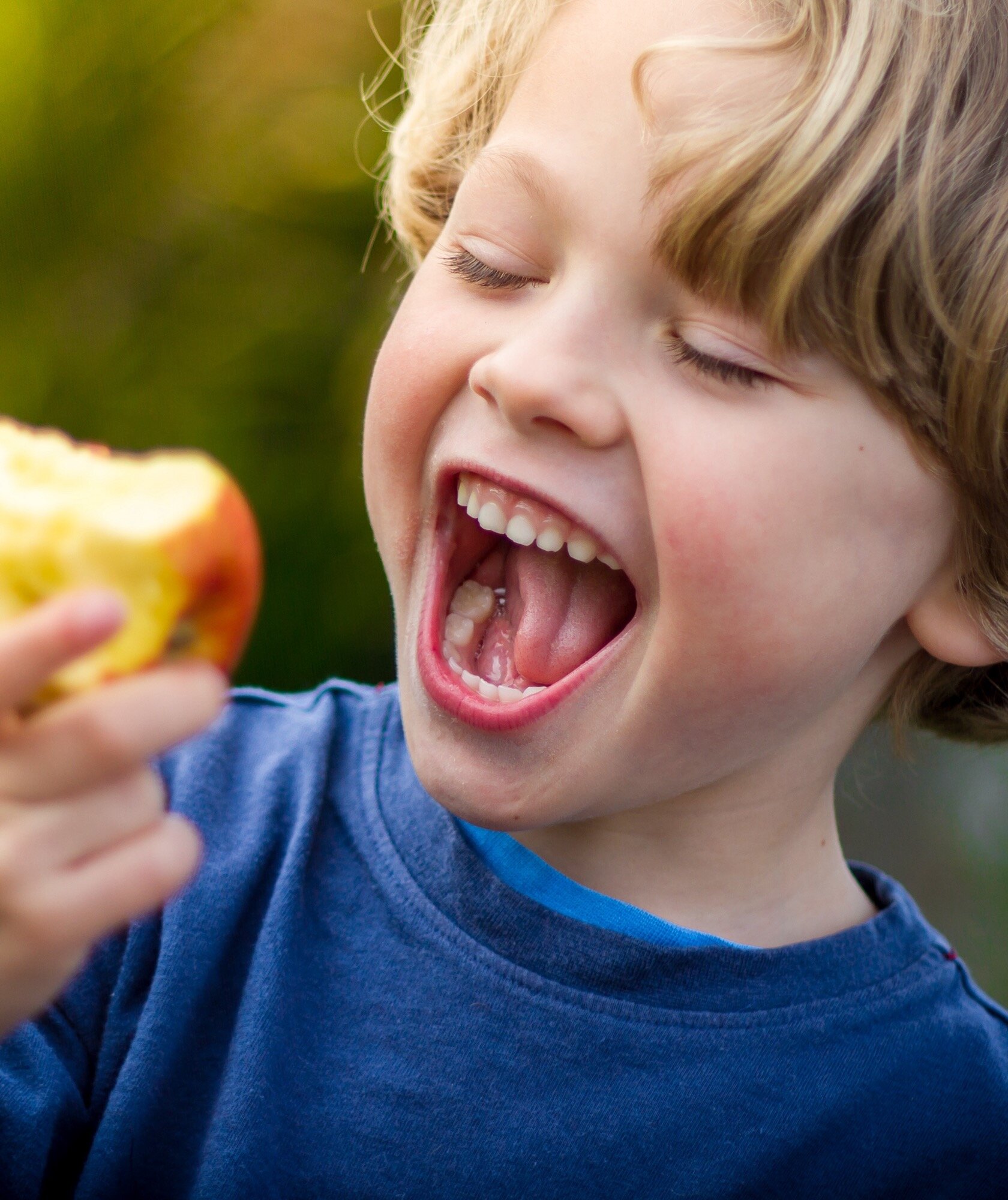 Laughing boy biting into an apple - convenient orthodontic care for West New York families